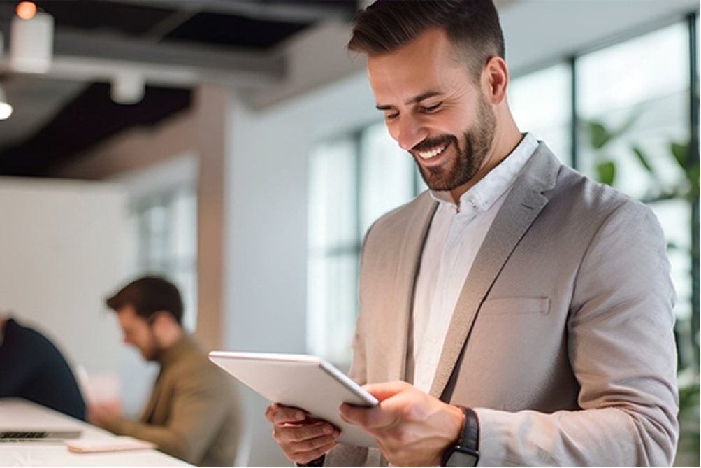 Hombre de traje beige muy bien puesto sosteniendo una tablet y sonriendo ampliamente