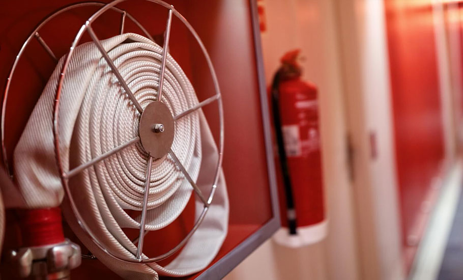 Primer plano de manguera de emergencia contra incendios descansando en su caja protectora en la pared