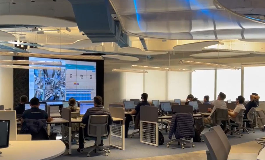 Panoramama de oficina de centro de operaciones con gente trabajando en sus respestivos escritorios al lado de pantalla gigante