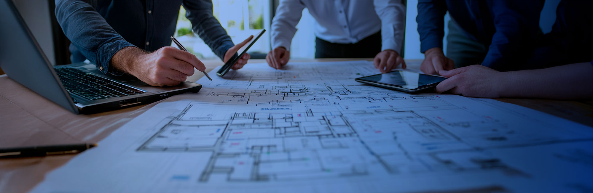 Ejecutivos haciendo anotaciones y planificando sobre enormes planos de construcciones desplegados en una mesa de trabajo